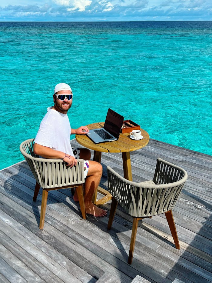 Man working on a laptop by the ocean, embodying remote work lifestyle.