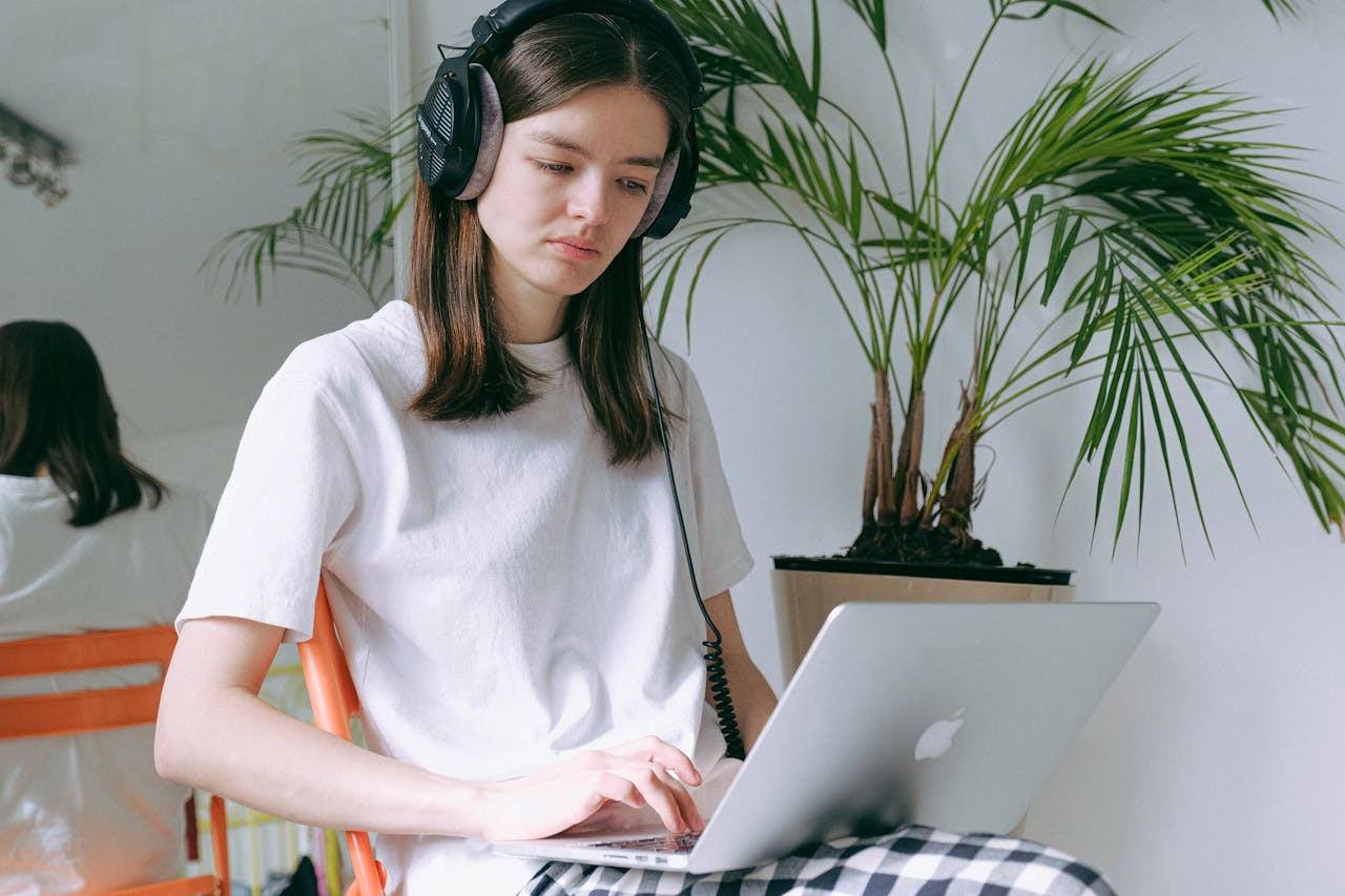 A young woman working remotely at home using a laptop and headphones, surrounded by indoor plants.